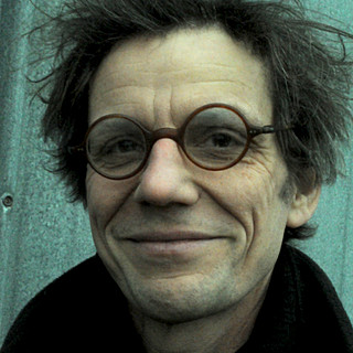 Im frontalen Porträt von Christof von Büren sticht seine schwarze runde Brille und sein breites Lächeln hervor. 